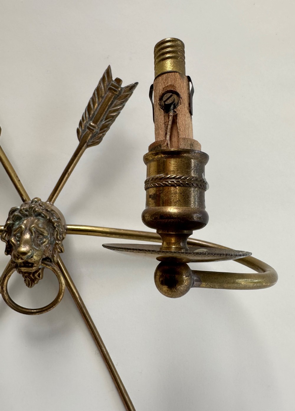A pair of French cast brass wall sconces featuring crossed arrow backplates centred by lion masks with ring handles and two curving candle arms. View IV