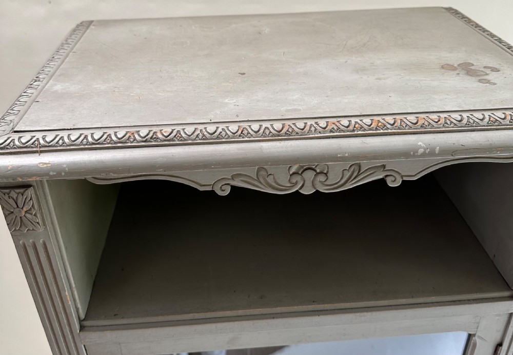 A tall grey-painted French provincial cabinet featuring an upper open compartment, a central glazed glass door, three lower drawers with ring handles, and fluted pilasters. View V