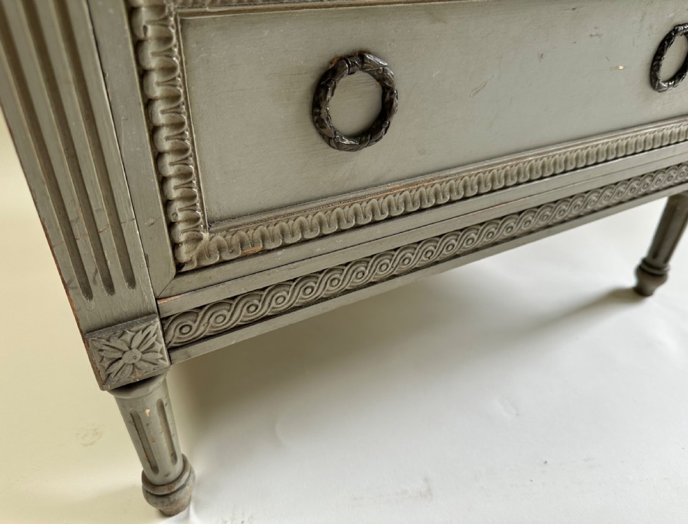 A tall grey-painted French provincial cabinet featuring an upper open compartment, a central glazed glass door, three lower drawers with ring handles, and fluted pilasters. View VII