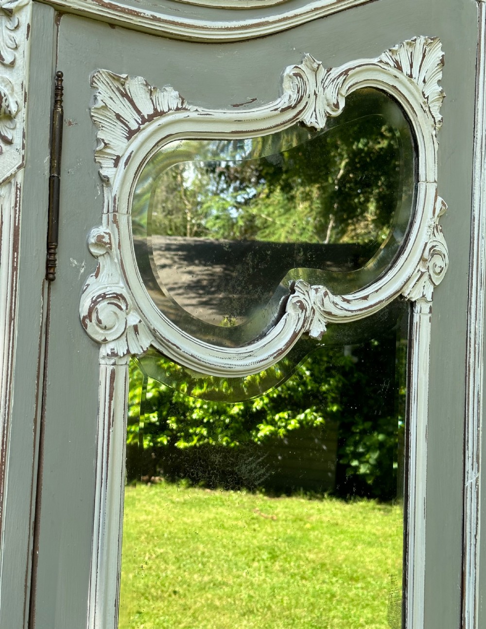 A tall grey and off-white painted French armoire featuring arched mirrored double doors, carved cresting at the top, and short cabriole legs. View IV