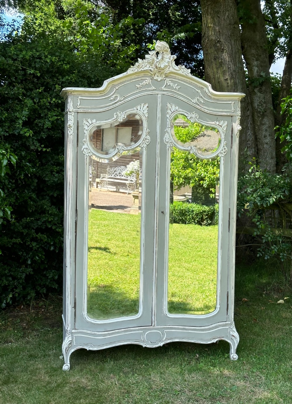 A tall grey and off-white painted French armoire featuring arched mirrored double doors, carved cresting at the top, and short cabriole legs. View V