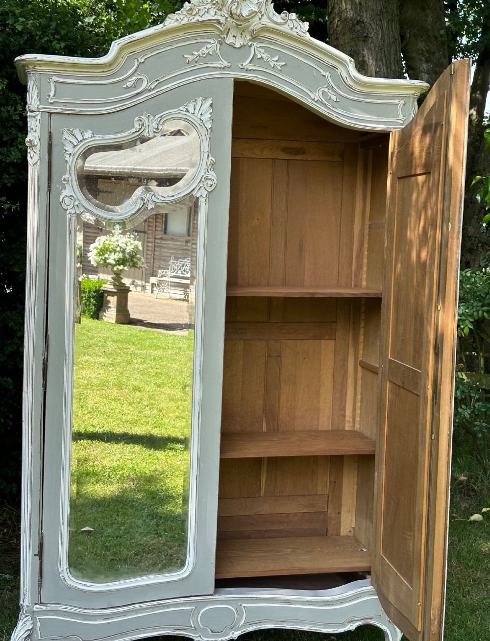 A tall grey and off-white painted French armoire featuring arched mirrored double doors, carved cresting at the top, and short cabriole legs. View IX