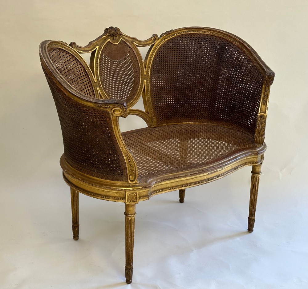 A Louis XVI style French giltwood sofa featuring a curved frame, hand-woven cane backrest and seat, and fluted legs.