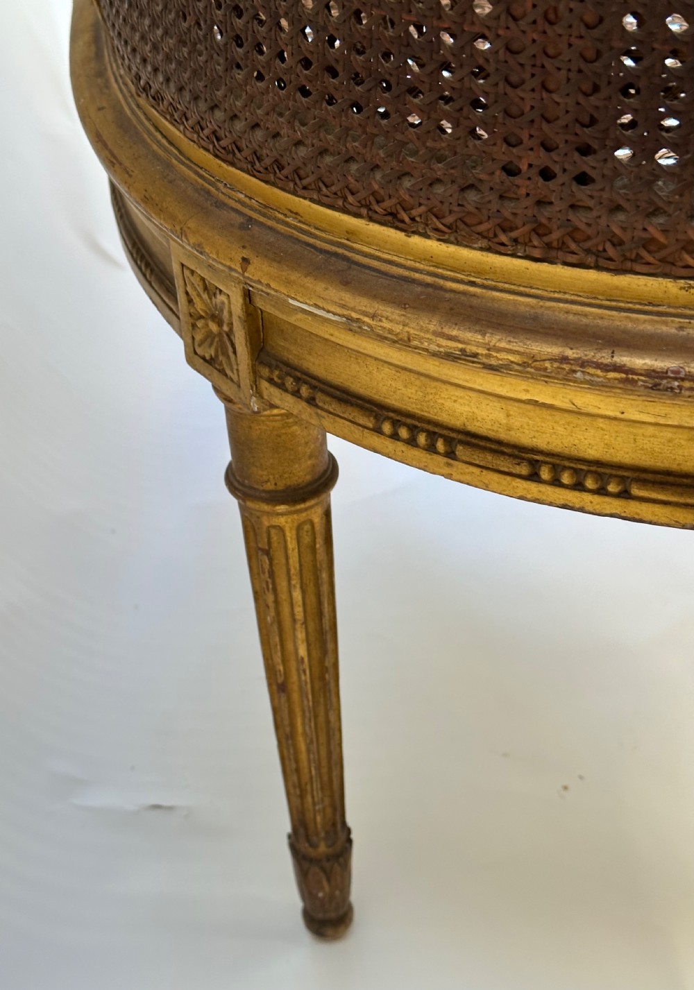 A Louis XVI style French giltwood sofa featuring a curved frame, hand-woven cane backrest and seat, and fluted legs. View VIII