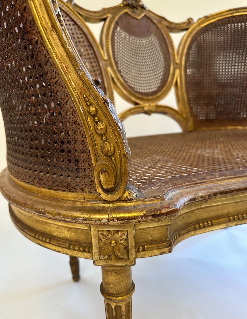 A Louis XVI style French giltwood sofa featuring a curved frame, hand-woven cane backrest and seat, and fluted legs. View XII