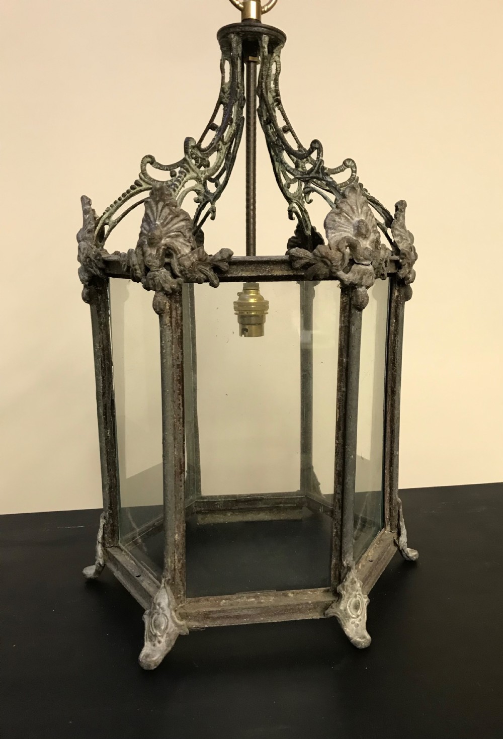 A hexagonal weathered metal hanging lantern featuring clear glass panels, an ornate pierced crown, and an internal brass bulb fitting.