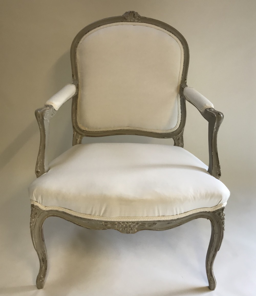 A French Louis XV style painted walnut armchair featuring cream fabric upholstery, padded armrests, carved cresting, and cabriole legs. View II