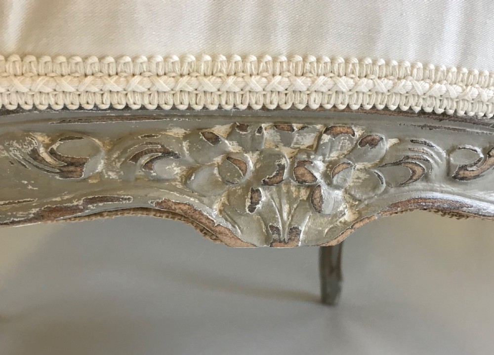 A French Louis XV style painted walnut armchair featuring cream fabric upholstery, padded armrests, carved cresting, and cabriole legs. View VI