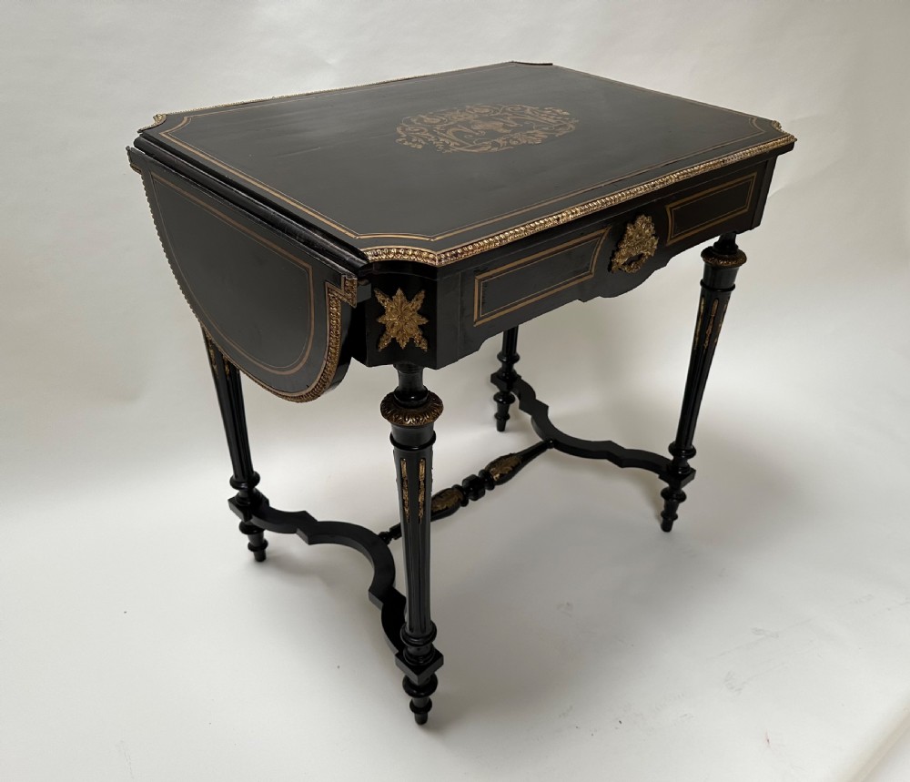 An ebonised Napoleon III drop-leaf table featuring gilt brass mounts, incised inlay, and turned legs joined by a curved stretcher.