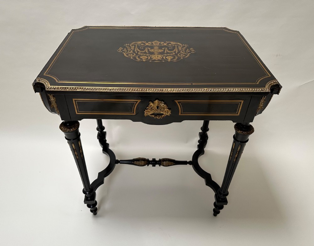 An ebonised Napoleon III drop-leaf table featuring gilt brass mounts, incised inlay, and turned legs joined by a curved stretcher. View III