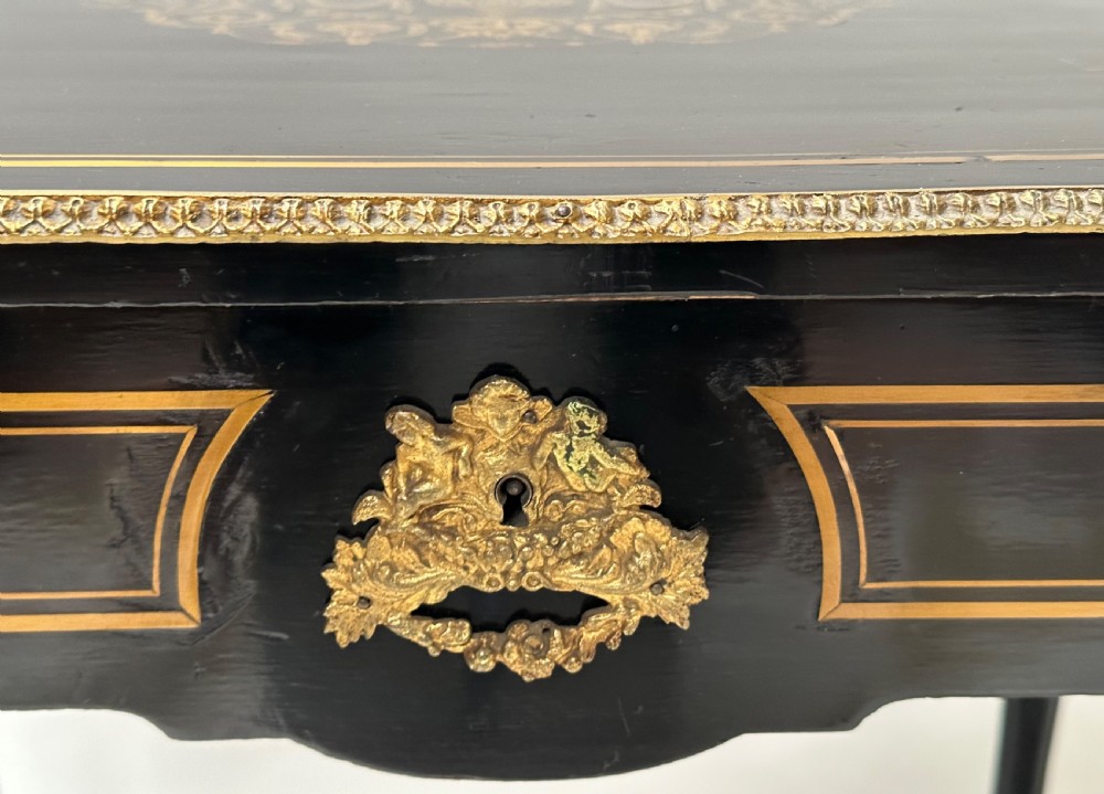 An ebonised Napoleon III drop-leaf table featuring gilt brass mounts, incised inlay, and turned legs joined by a curved stretcher. View X