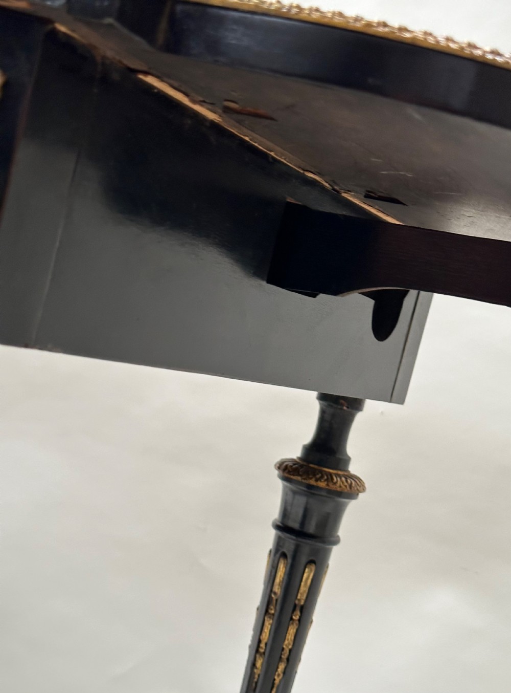 An ebonised Napoleon III drop-leaf table featuring gilt brass mounts, incised inlay, and turned legs joined by a curved stretcher. View XII