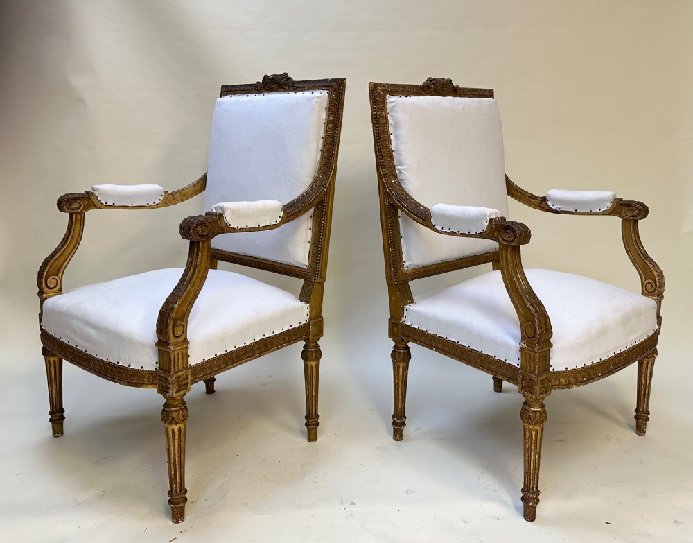 A pair of French Louis XVI style giltwood armchairs with carved square backs, padded armrests, and white fabric upholstery. View II