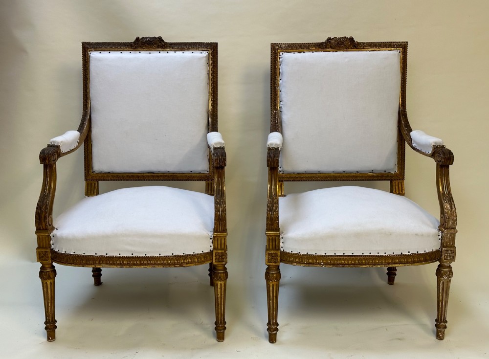 A pair of French Louis XVI style giltwood armchairs with carved square backs, padded armrests, and white fabric upholstery. View III