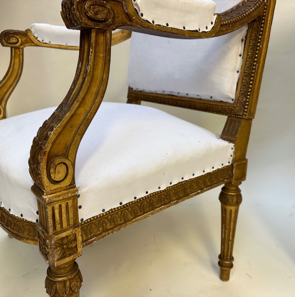 A pair of French Louis XVI style giltwood armchairs with carved square backs, padded armrests, and white fabric upholstery. View VII