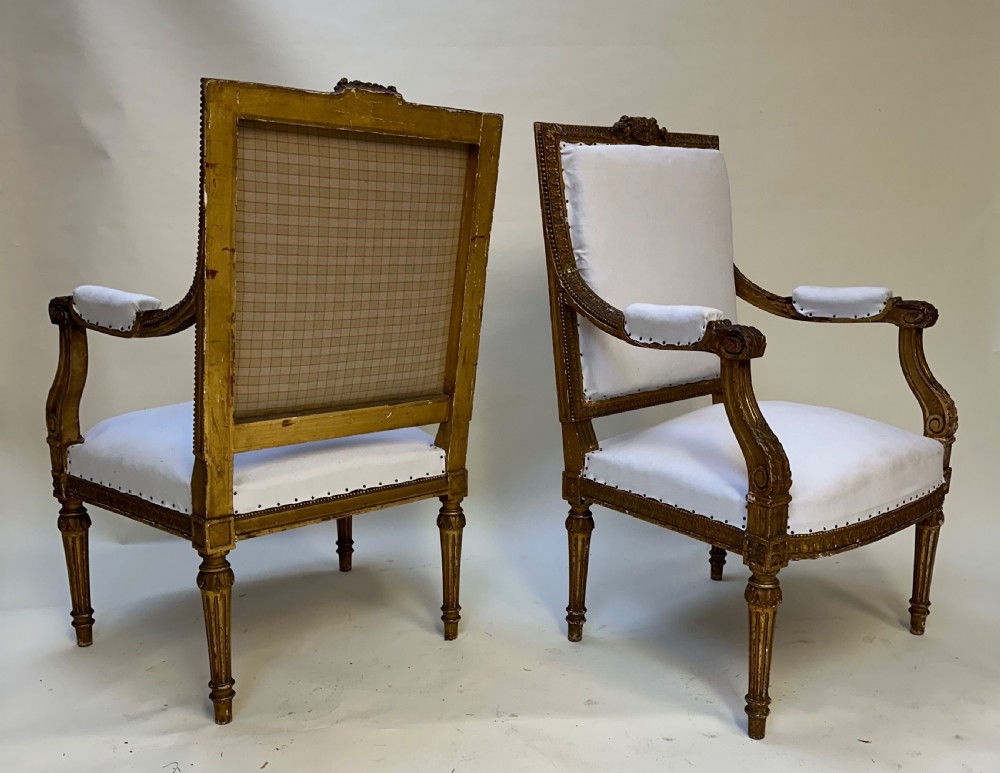 A pair of French Louis XVI style giltwood armchairs with carved square backs, padded armrests, and white fabric upholstery. View VIII