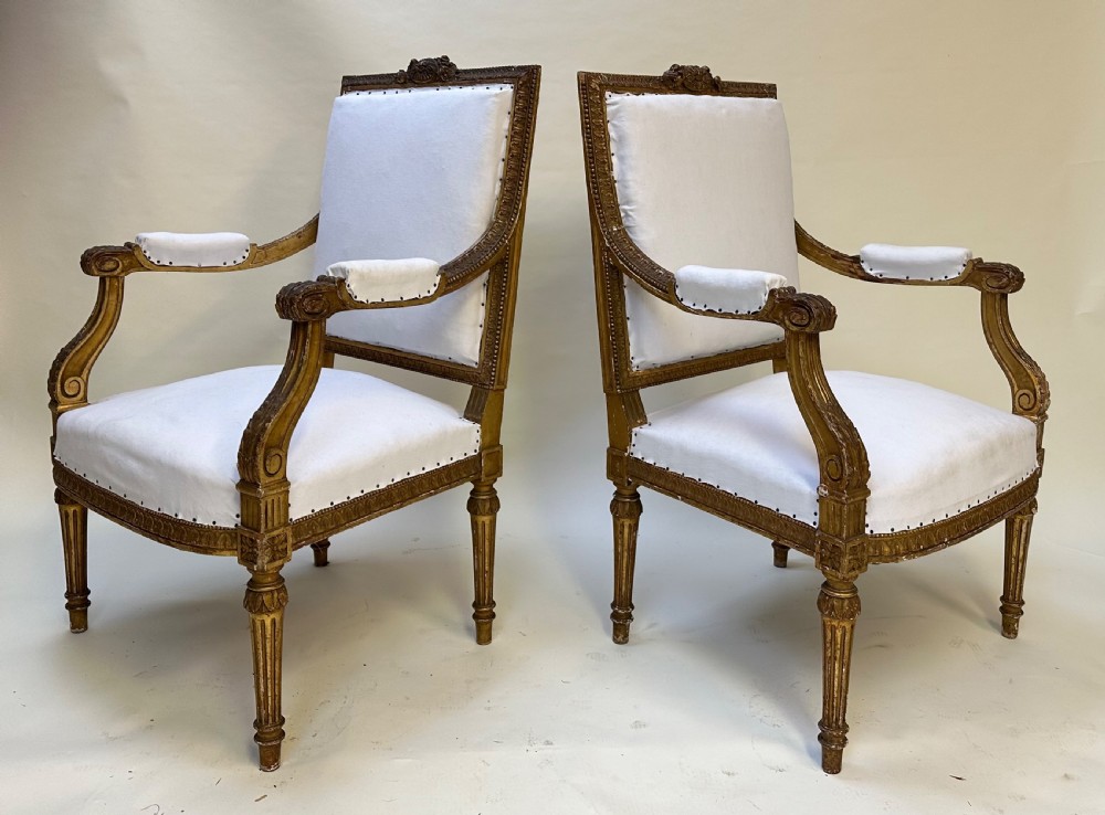 A pair of French Louis XVI style giltwood armchairs with carved square backs, padded armrests, and white fabric upholstery. View X