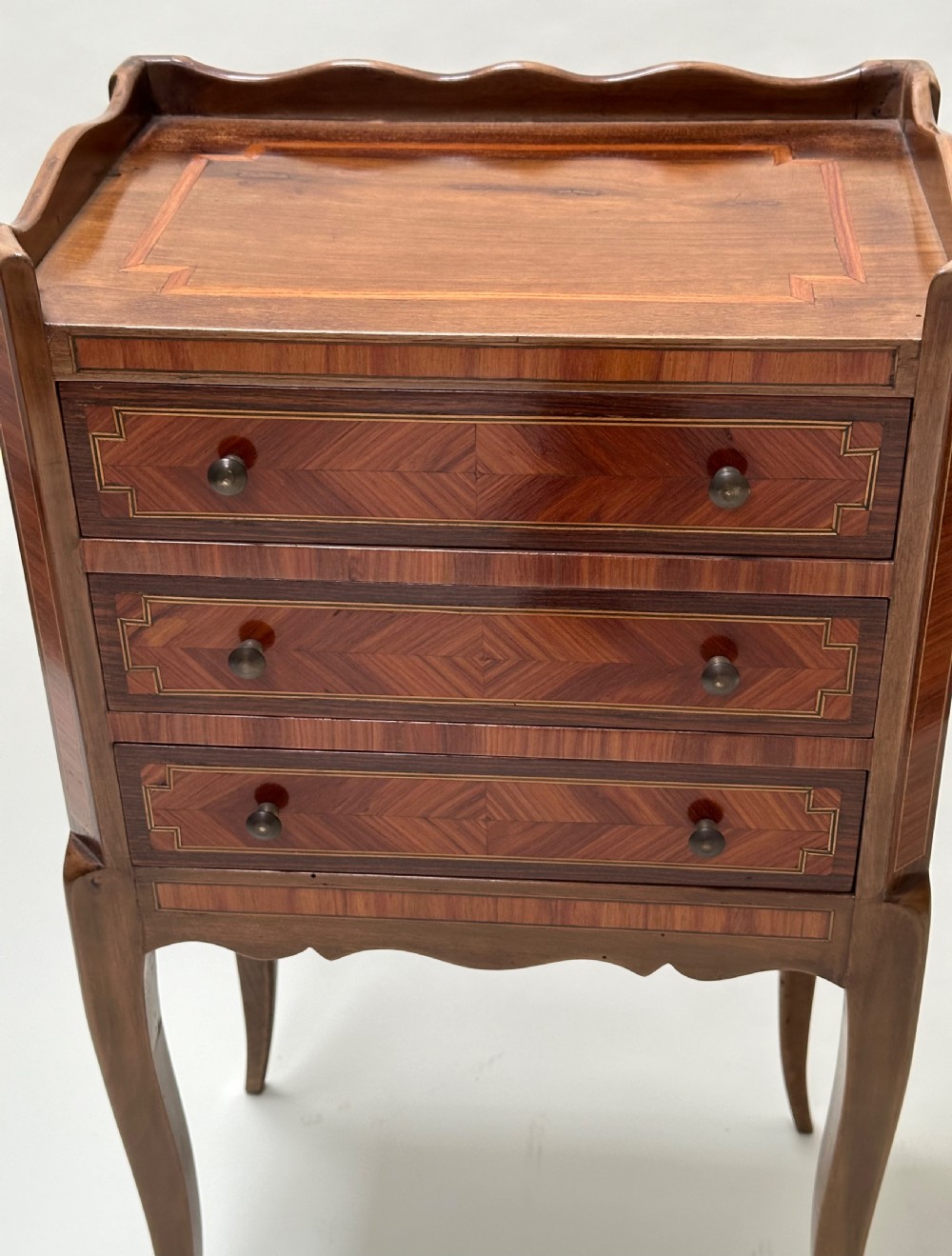 A pair of French Louis XV style warm brown walnut bedside tables featuring geometric parquetry inlay, shaped galleries, and slender cabriole legs. View IV