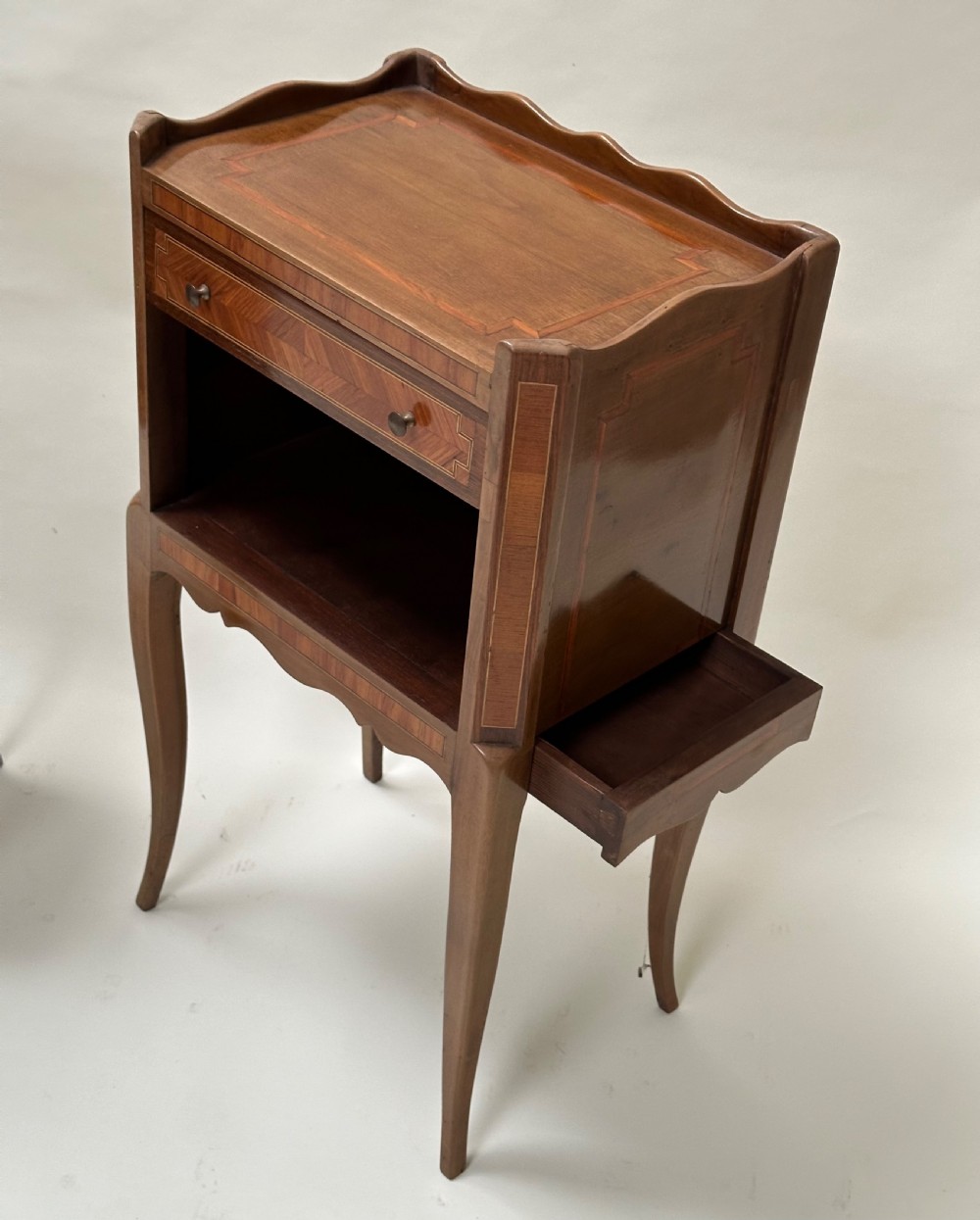 A pair of French Louis XV style warm brown walnut bedside tables featuring geometric parquetry inlay, shaped galleries, and slender cabriole legs. View V
