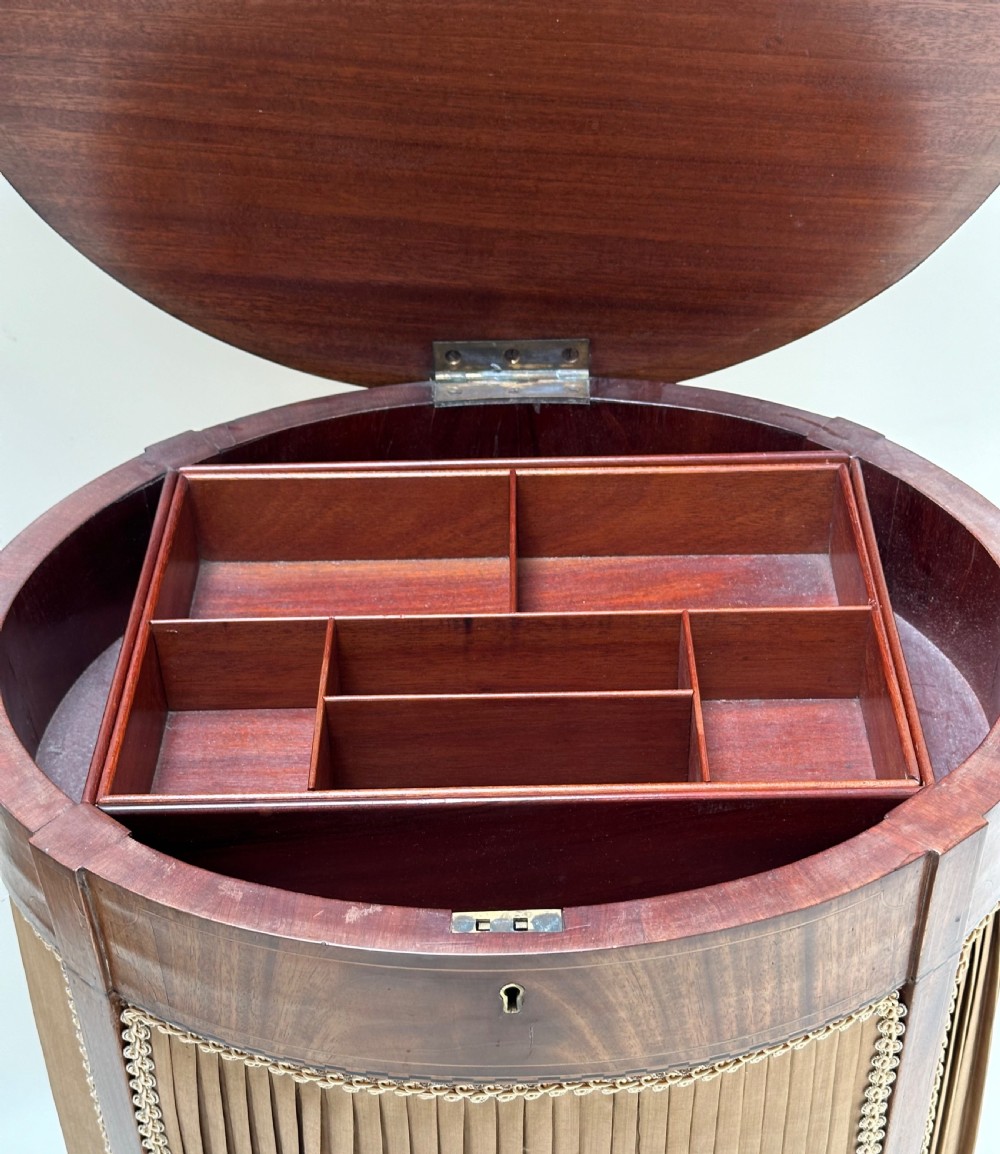 A round antique sewing table featuring a radial walnut veneer top with marquetry inlay, supported by a pleated tan silk basket and slender curved legs. View VI
