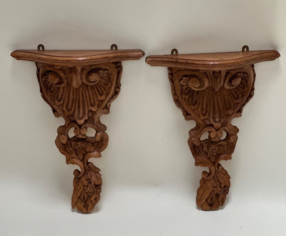 A matching pair of hand-carved warm brown wooden wall brackets featuring ornate scrollwork, shell fluting, and floral motifs. View II