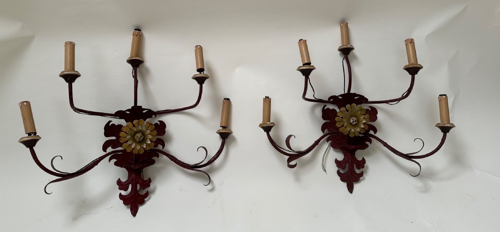 A pair of large French wrought iron five-light wall sconces finished in dark red paint with central gilt floral rosettes and sweeping scrolling arms.