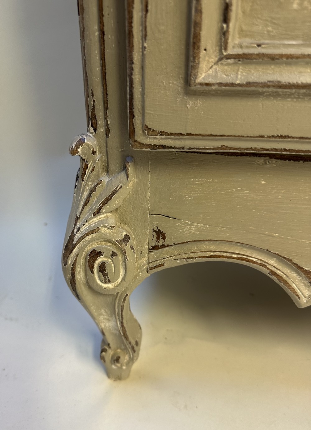 A tall French provincial glazed cabinet featuring a distressed grey painted finish, multi-pane glass doors, intricate scroll carving at the base, and short cabriole legs. View IV