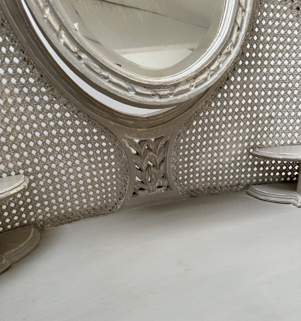 A grey painted French style dressing table with a cane back panel, oval top mirror, small side drawers, and slender carved legs. View VI