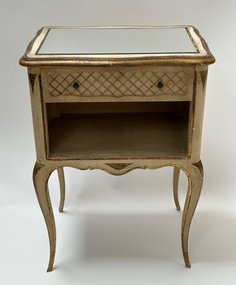A pair of cream and gold Florentine bedside tables featuring mirrored tops, open lower compartments, carved lattice drawers, and slender cabriole legs. View VII