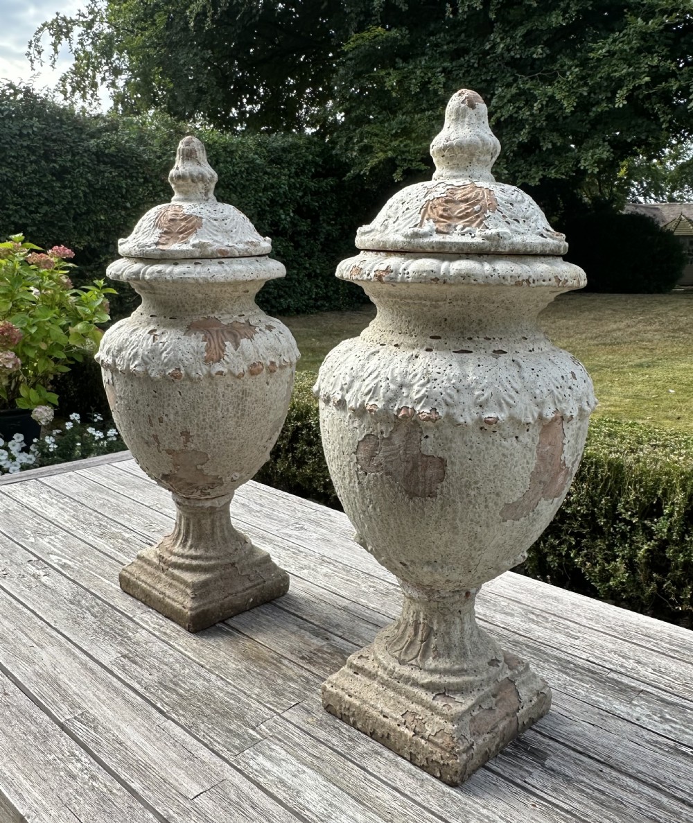 A pair of weathered white painted terracotta urns featuring relief leaf carving, finial lids, and square pedestal bases. View III