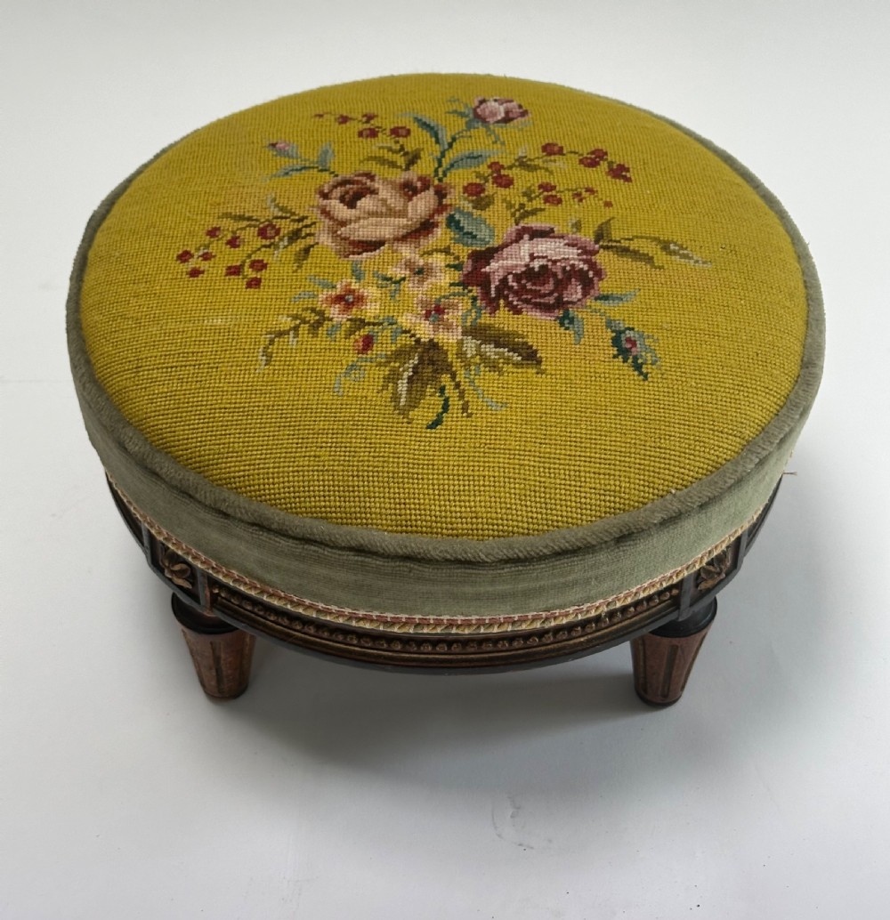 A low circular French footstool featuring a floral needlepoint seat in mustard yellow with green velvet trim and carved wooden legs. View III