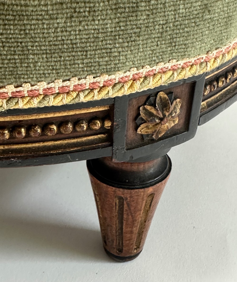 A low circular French footstool featuring a floral needlepoint seat in mustard yellow with green velvet trim and carved wooden legs. View V