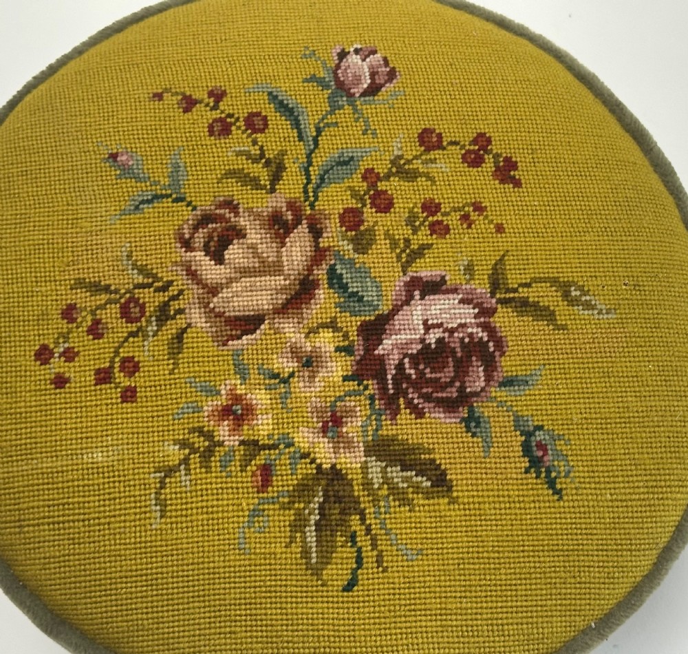 A low circular French footstool featuring a floral needlepoint seat in mustard yellow with green velvet trim and carved wooden legs. View IX