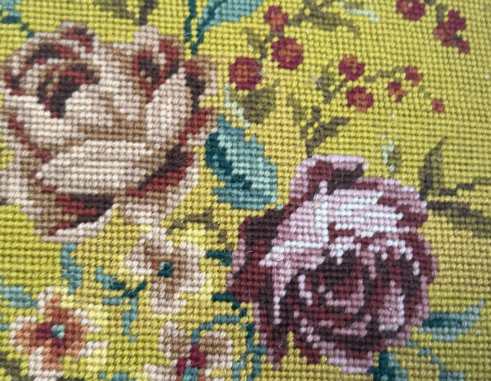 A low circular French footstool featuring a floral needlepoint seat in mustard yellow with green velvet trim and carved wooden legs. View X