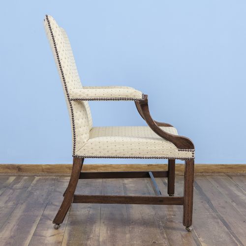 A George III mahogany Gainsborough armchair featuring patterned cream upholstery, brass tack trim, carved serpentine arm supports, and straight legs with brass castors. View V
