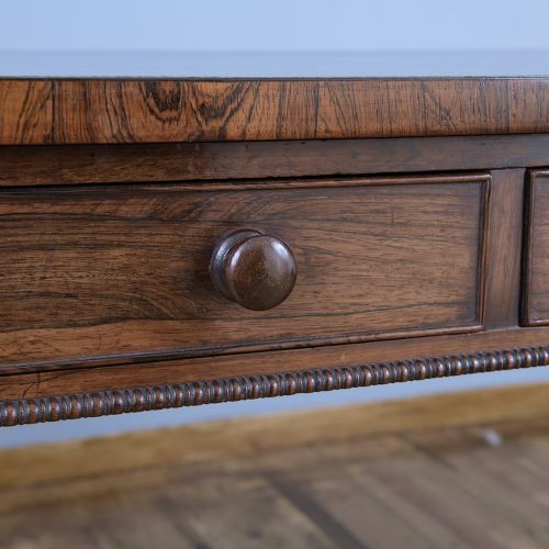 fig 1. A Regency rosewood writing desk featuring a black leather inset surface, frieze drawers, and carved trestle end supports on brass castors.