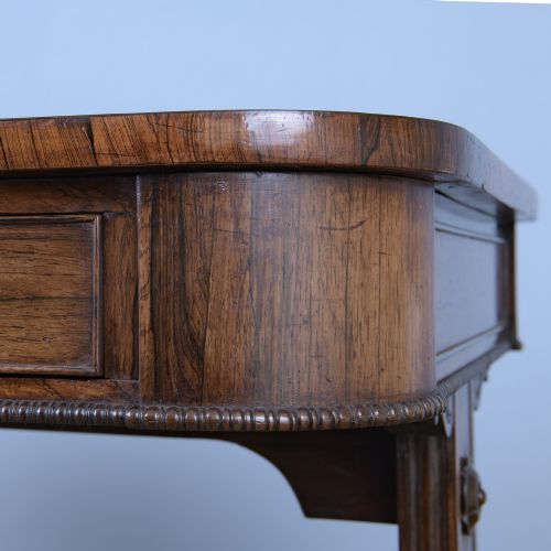 fig 2. A Regency rosewood writing desk featuring a black leather inset surface, frieze drawers, and carved trestle end supports on brass castors.