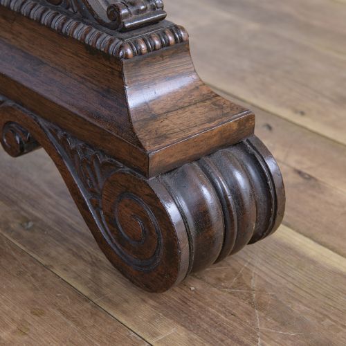 fig 3. A Regency rosewood writing desk featuring a black leather inset surface, frieze drawers, and carved trestle end supports on brass castors.