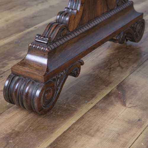 A Regency rosewood writing desk featuring a black leather inset surface, frieze drawers, and carved trestle end supports on brass castors. View V