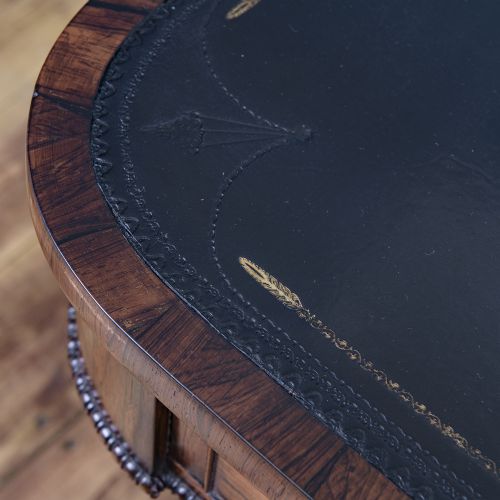 A Regency rosewood writing desk featuring a black leather inset surface, frieze drawers, and carved trestle end supports on brass castors. View VI