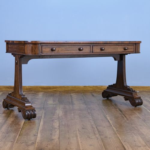 A Regency rosewood writing desk featuring a black leather inset surface, frieze drawers, and carved trestle end supports on brass castors. View VIII