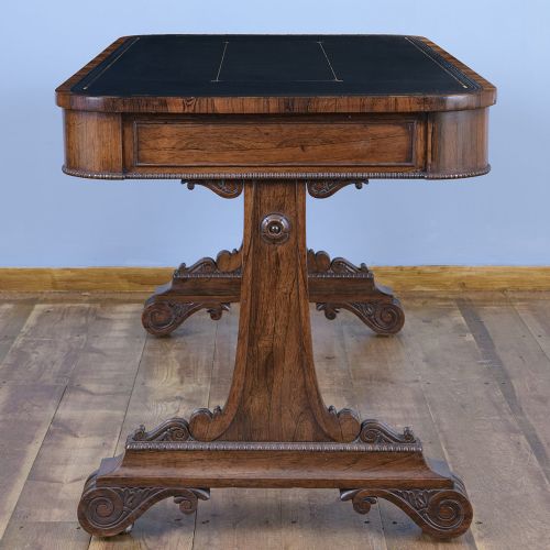 A Regency rosewood writing desk featuring a black leather inset surface, frieze drawers, and carved trestle end supports on brass castors. View IX