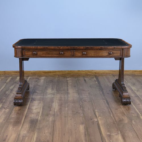 A Regency rosewood writing desk featuring a black leather inset surface, frieze drawers, and carved trestle end supports on brass castors.