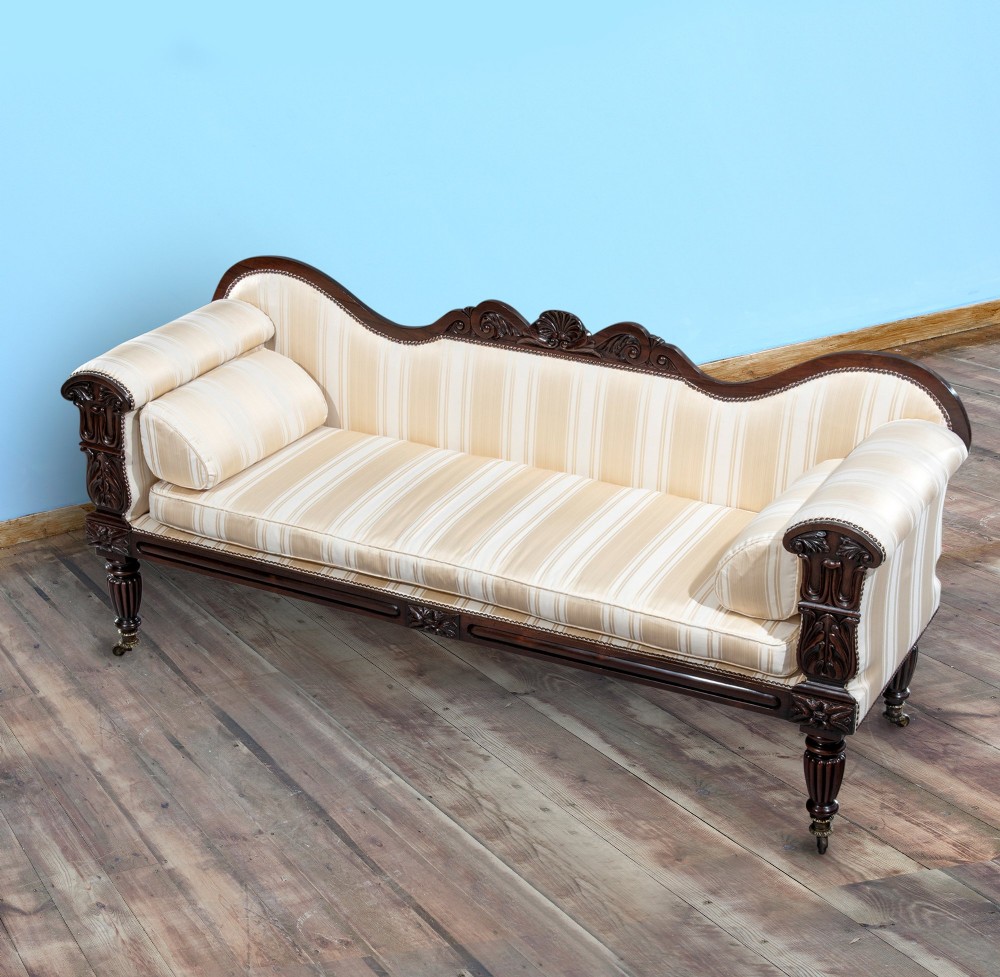 A matching pair of 19th-century dark rosewood sofas with carved cresting, scroll arms, reeded legs on brass castors, and cream striped fabric upholstery. View II