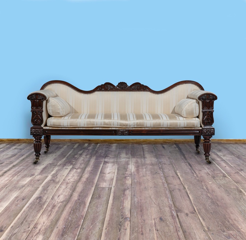 A matching pair of 19th-century dark rosewood sofas with carved cresting, scroll arms, reeded legs on brass castors, and cream striped fabric upholstery. View III