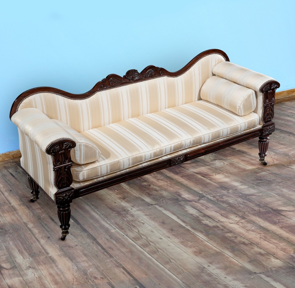 A matching pair of 19th-century dark rosewood sofas with carved cresting, scroll arms, reeded legs on brass castors, and cream striped fabric upholstery. View IV