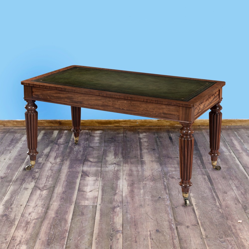 A nineteenth-century mahogany writing table featuring a green leather top, fluted turned legs, and brass castors.