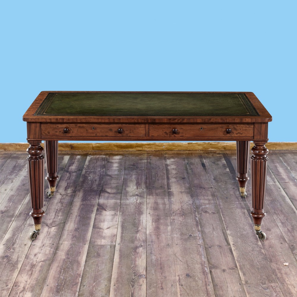 A nineteenth-century mahogany writing table featuring a green leather top, fluted turned legs, and brass castors. View II