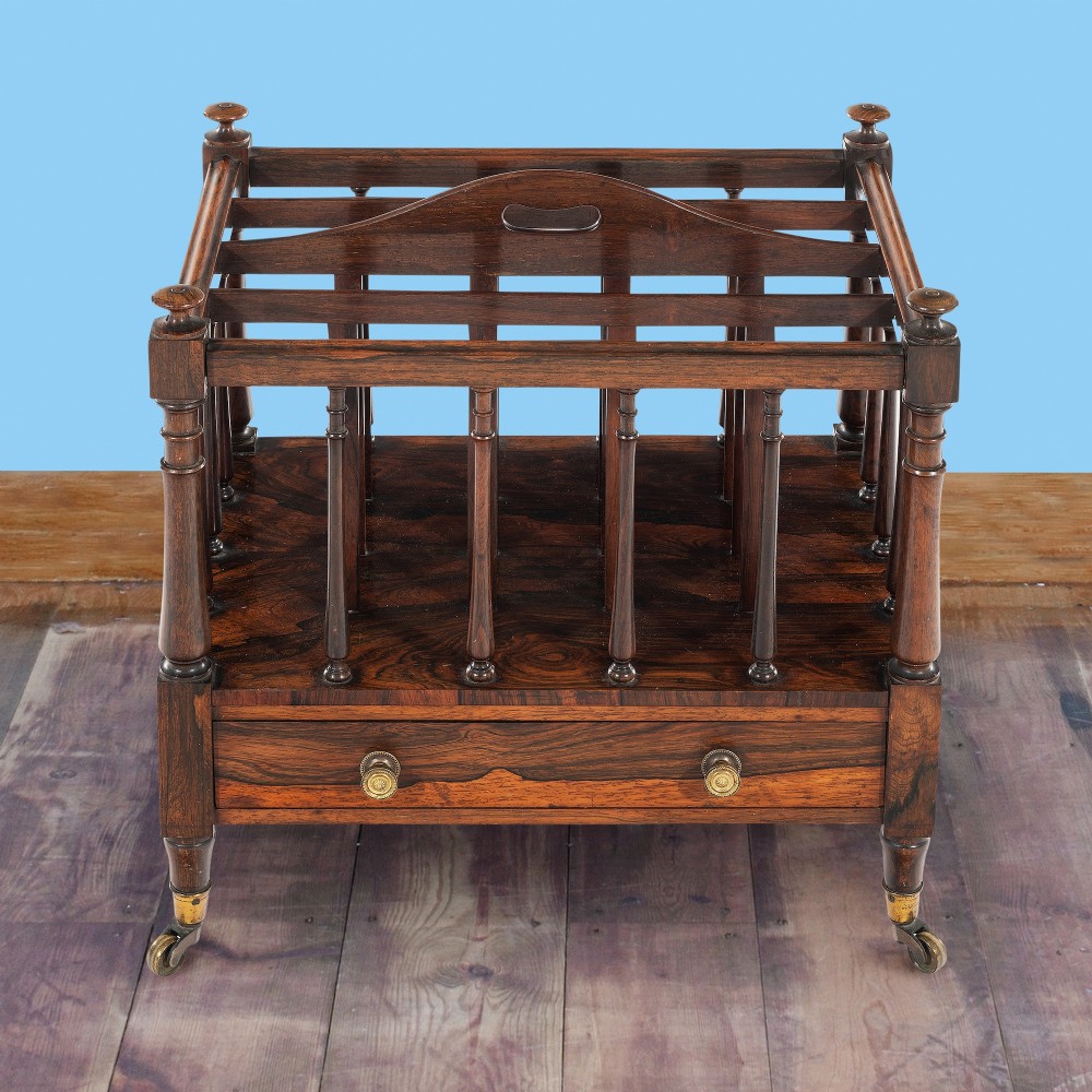 A Victorian rosewood music canterbury featuring turned spindle dividers, a top carrying handle, a lower drawer with two brass knobs, and turned legs with brass castors. View II