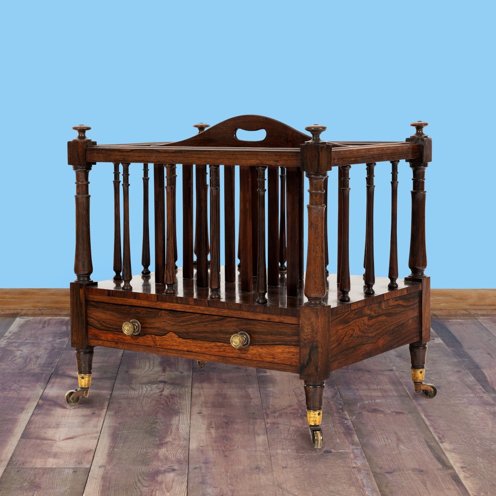 A Victorian rosewood music canterbury featuring turned spindle dividers, a top carrying handle, a lower drawer with two brass knobs, and turned legs with brass castors. View IV